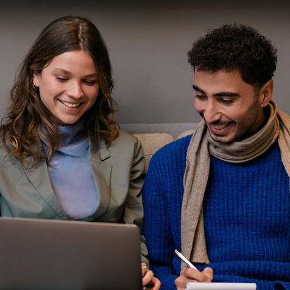 A man and woman seated on a sofa, engrossed in their work on a laptop computer.