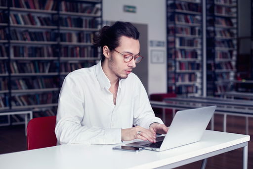 arten-der-promotion.jpg Ein Doktorand am Laptop in einer Bibliothek