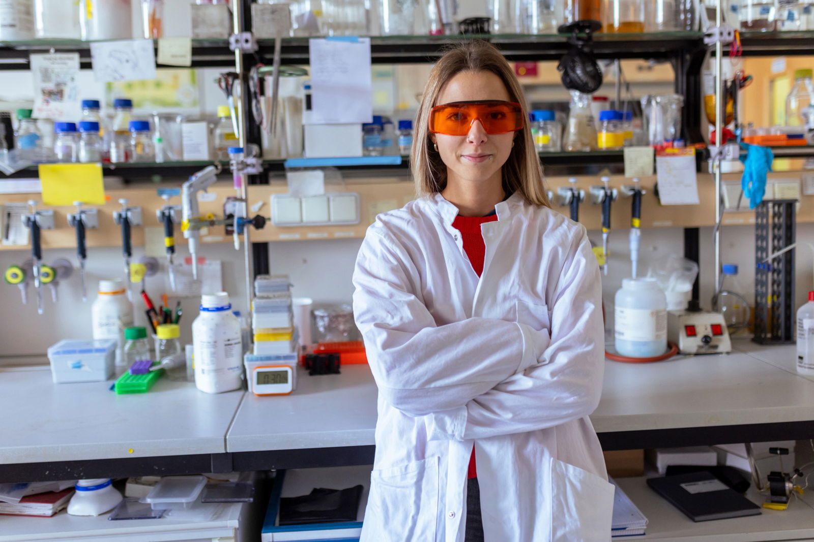 Eine junge Naturwissenschaftlerin mit Schutzbrille zufrieden lächelnd in einem Labor