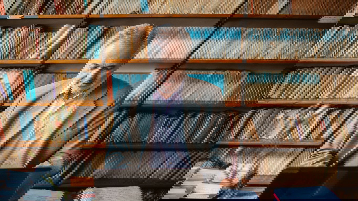 Digital Humanities_iStock-1369630989.jpg Digital Humanities: Ein Mann in einer Bibliothek mit alten Büchern am Laptop