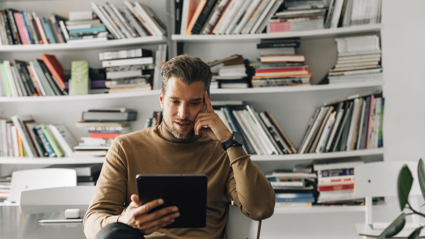 dissertation-veroeffentlichen.jpg Ein junger Mann mit Tablet vor einem Bücherregal