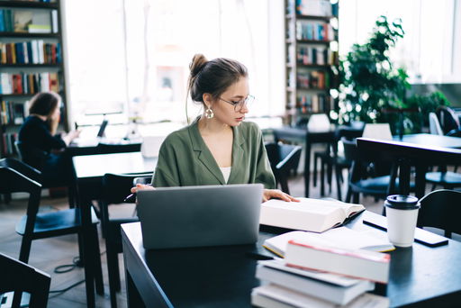 dissertation.jpg Eine Doktorandin am Tisch mit vielen Büchern schreibt an ihrer Dissertation