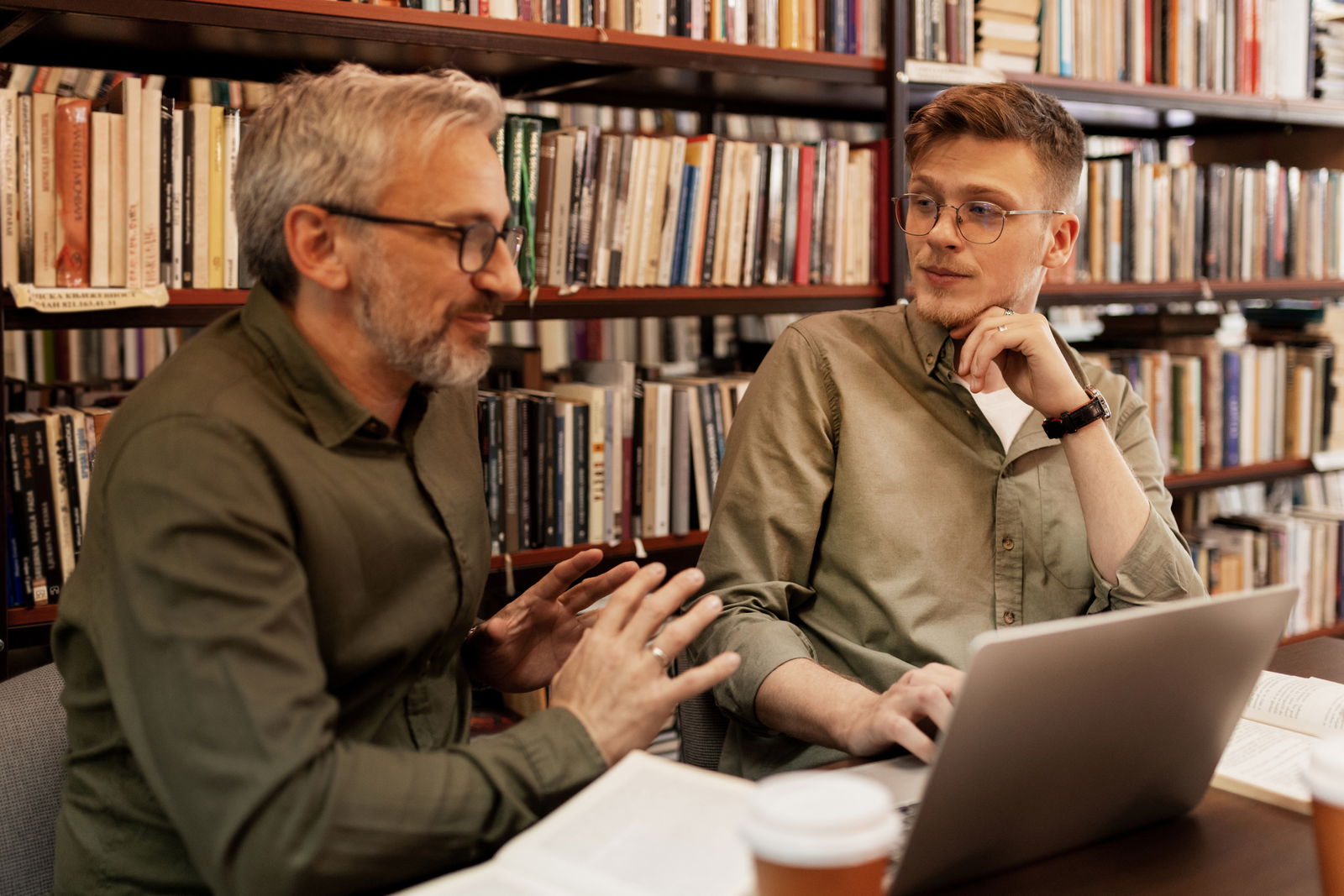 Ein blonder Student mit seinem Doktorvater bei einer Besprechung in einer Bibliothek
