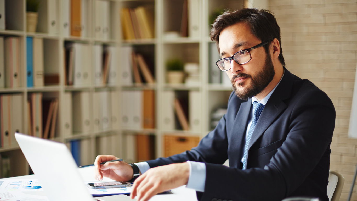 forschungsmanagement.jpg Ein Forschungsmanager mit Brille und dunklem Vollbart am Laptop in seinem Büro