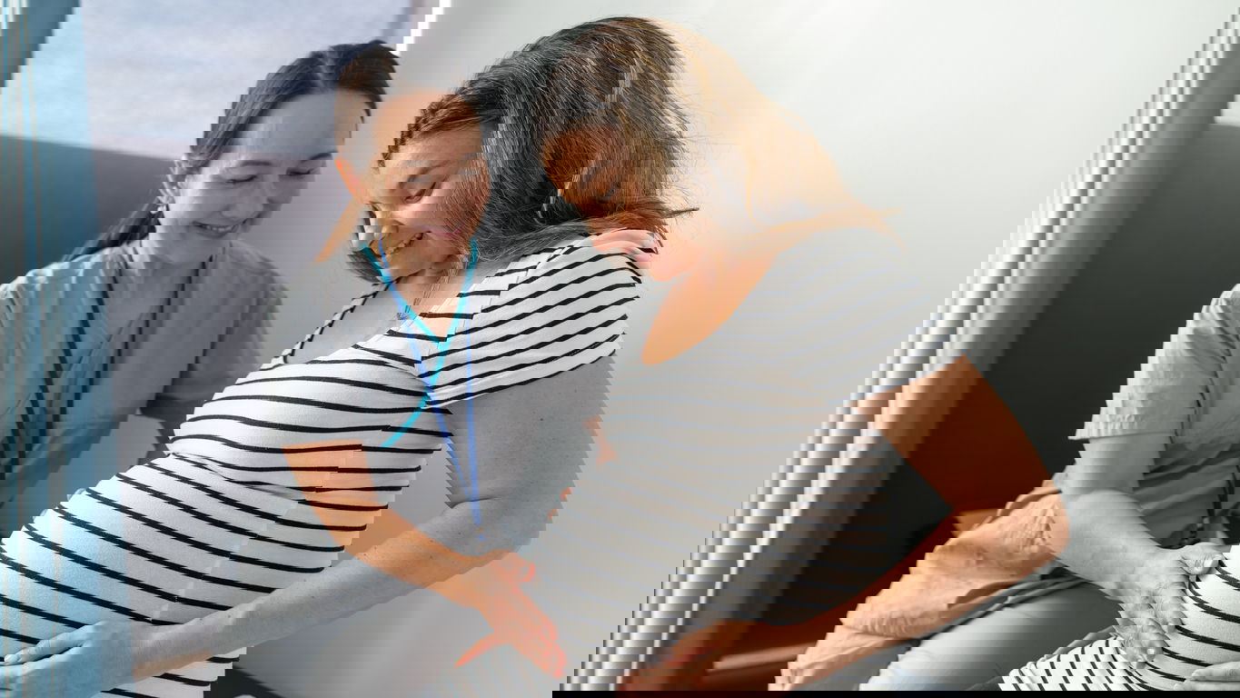 hebamme.jpg Eine Hebamme versorgt eine lächelnde schwangere Frau