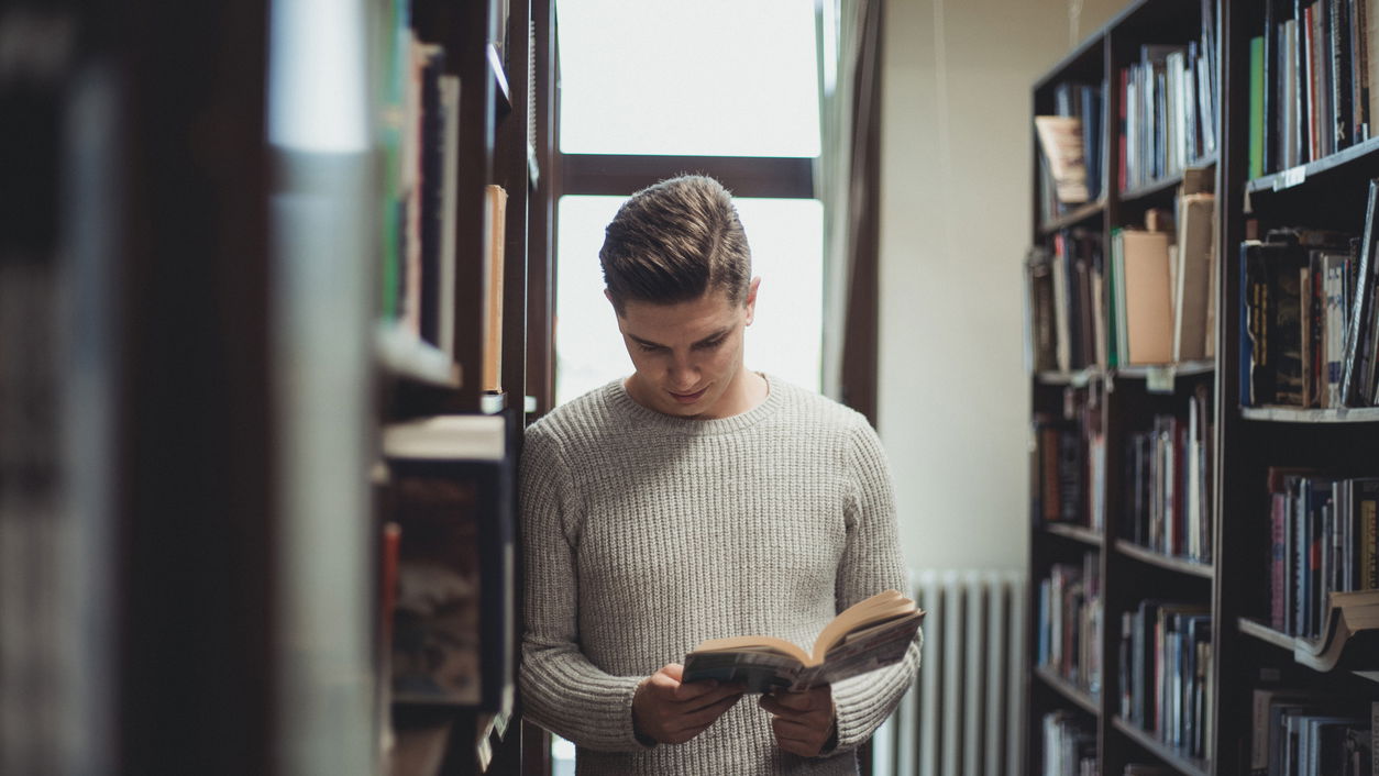 iStock-1332686502.jpg Ein Linguist blättert in einem Buch in einer Bibliothek