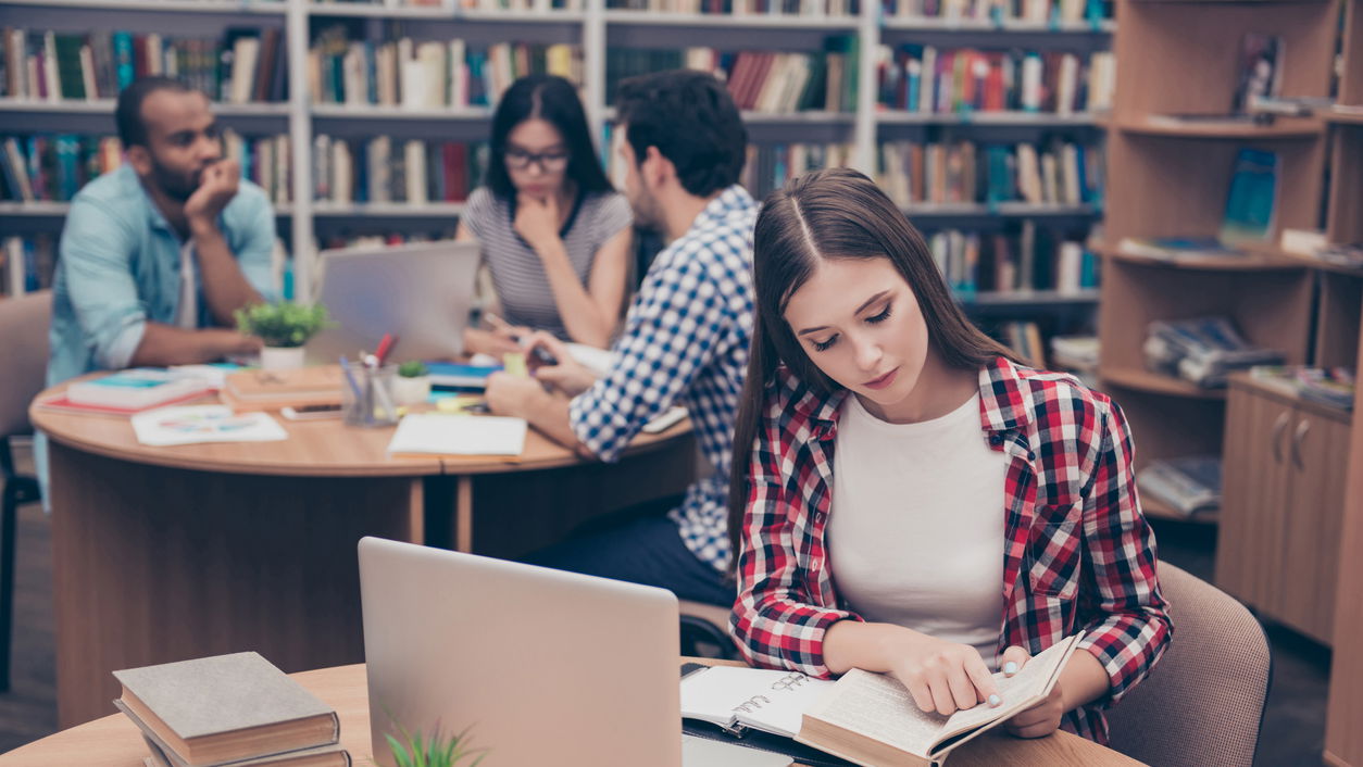 iStock-928932658.jpg Literaturwissenschaft studieren: Frau mit Buch in einer Uni-Bibliothek
