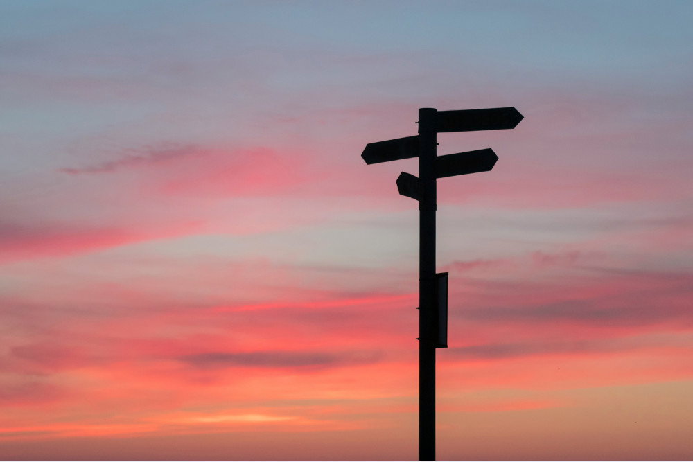Wegweiser, die in verschiedene Richtungen zeigen, vor Abendhimmel
