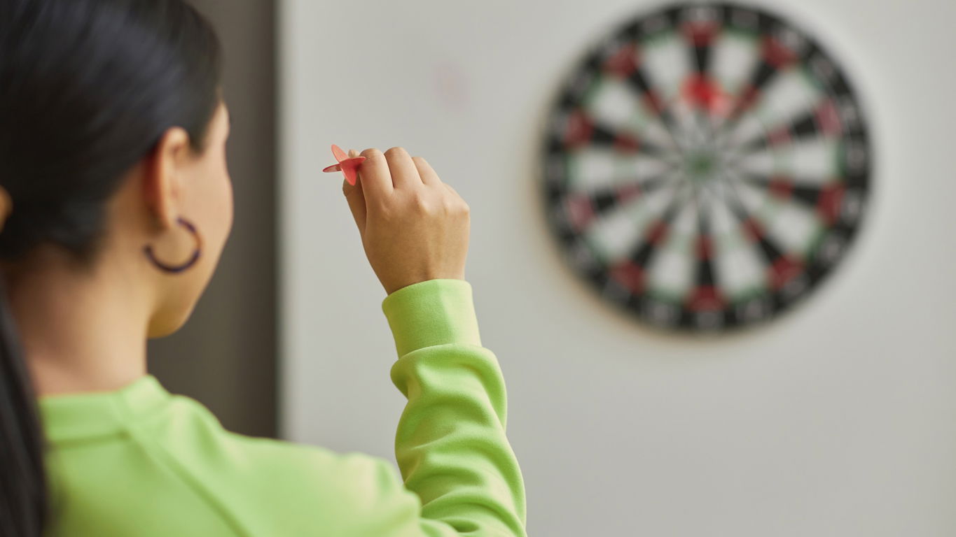 karriereziele.jpg Eine Frau in hellgrünem Pulli zielt mit einem Dartpfeil auf eine Dartscheibe