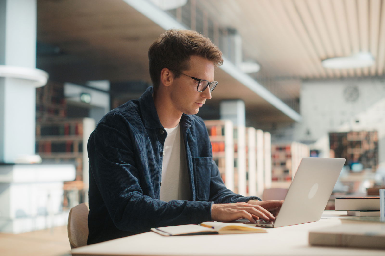 Ein junger Lehrer in einer Bibliothek am Laptop