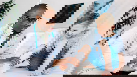 medizin-gehalt.jpg Ein dunkelhäutiger Arzt untersucht den eingegipsten Fuß eines Jungen