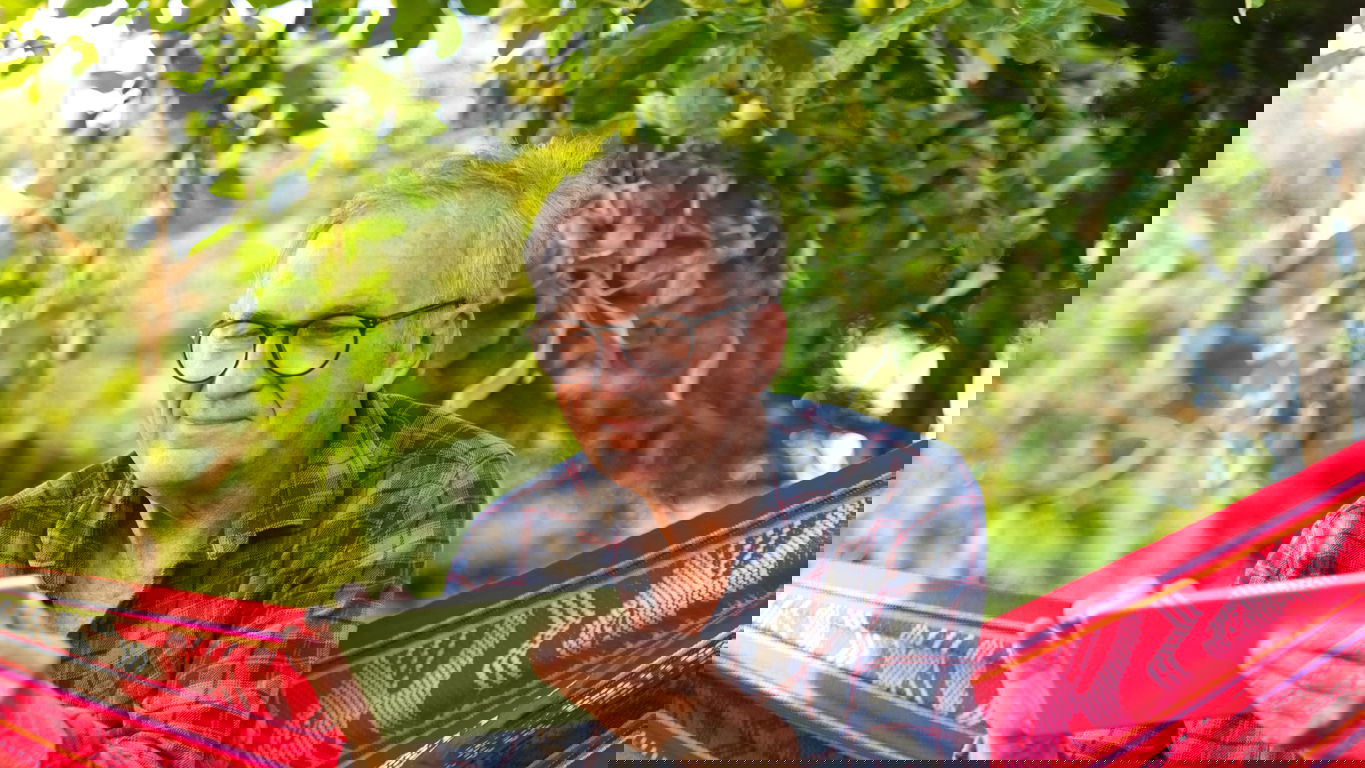 professor-im-ruhestand.jpg Ein emeritierter Professor mit Tablet in einer roten Hängematte im Garten