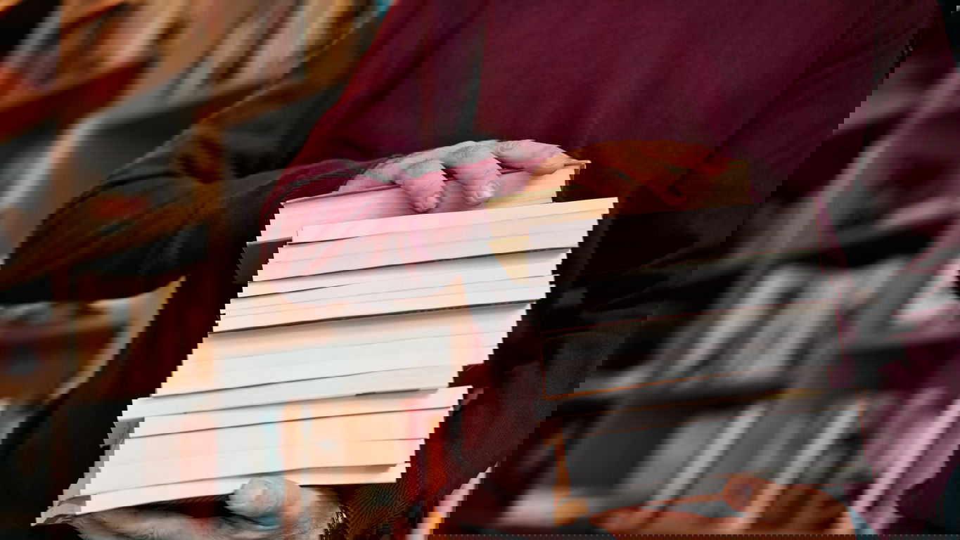 publikation.jpg Ein Mann trägt in einer Bibliothek einen Stapel Publikationen