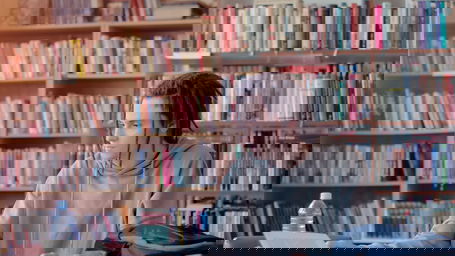 wissenschaftlicher-mitarbeiter-gehalt.jpg Ein Wissenschaftlicher Mitarbeiter mit dunklen Dreadlocks an einem Schreibtisch in der Bibliothek